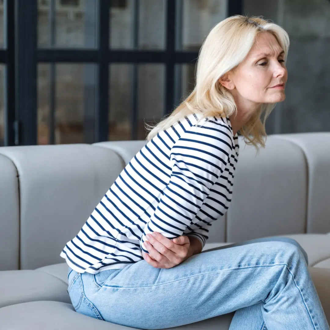 Woman sitting on a couch with a concerned expression, holding her bloating stomach.