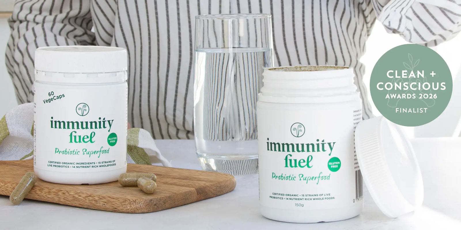 Two containers of 'immunity fuel' on a table with a glass of water and a person in the background.