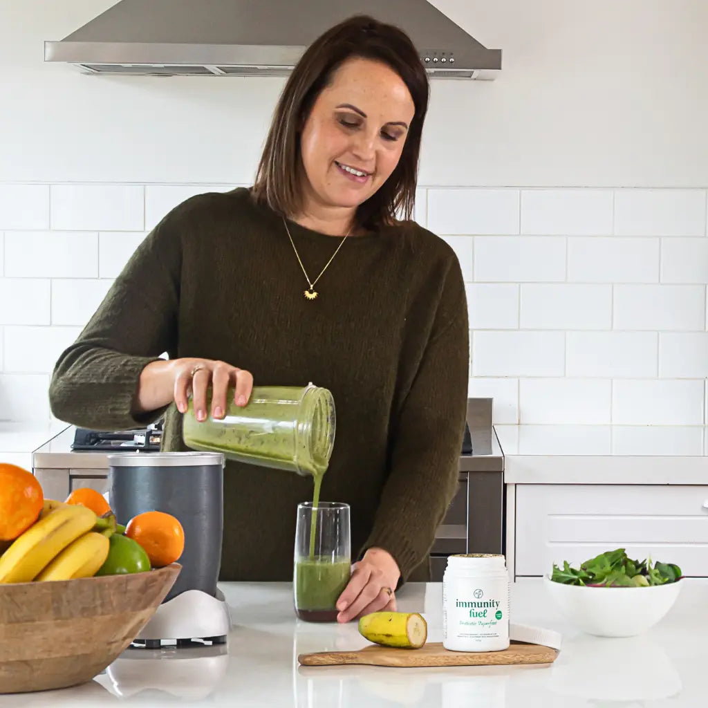 Happy woman making healthy green smoothie with immunity fuel gluten free probiotic powder
