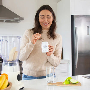 Happy Healthy Woman holding immunity fuel container in a kitchen with a blender and fruits on the counter.