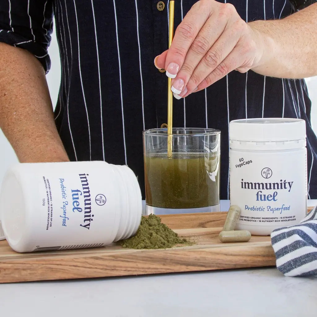 Person preparing a green drink with 'immunity fuel' supplement on a wooden board.