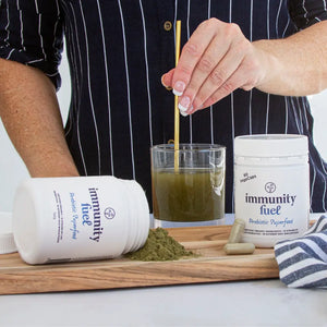 Stirring a healthy green drink with 'immunity fuel' supplement containers on a wooden board.