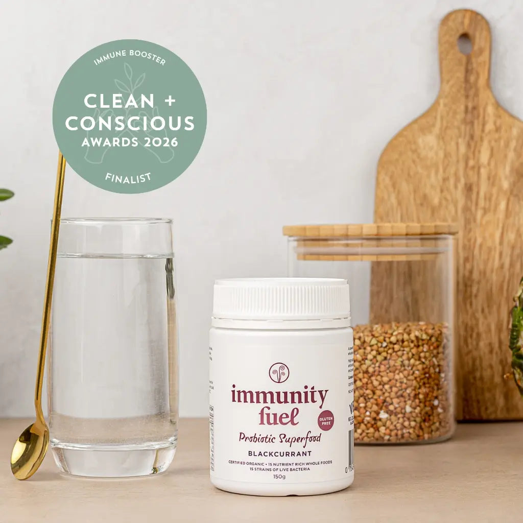 Jar of 'immunity fuel' probiotic superfood with a glass of water and wooden cutting board on a light surface.
