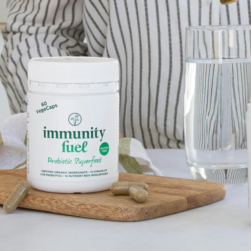 Container of 'immunity fuel' probiotic supplement on a wooden board with a glass of water in the background.